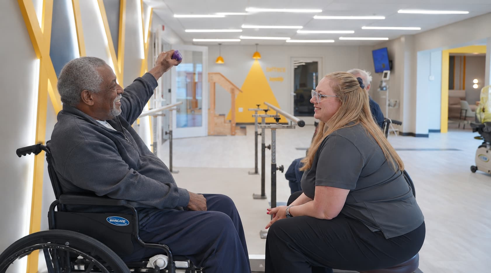A resident working with a weight beside a therapist in the rehab gym
